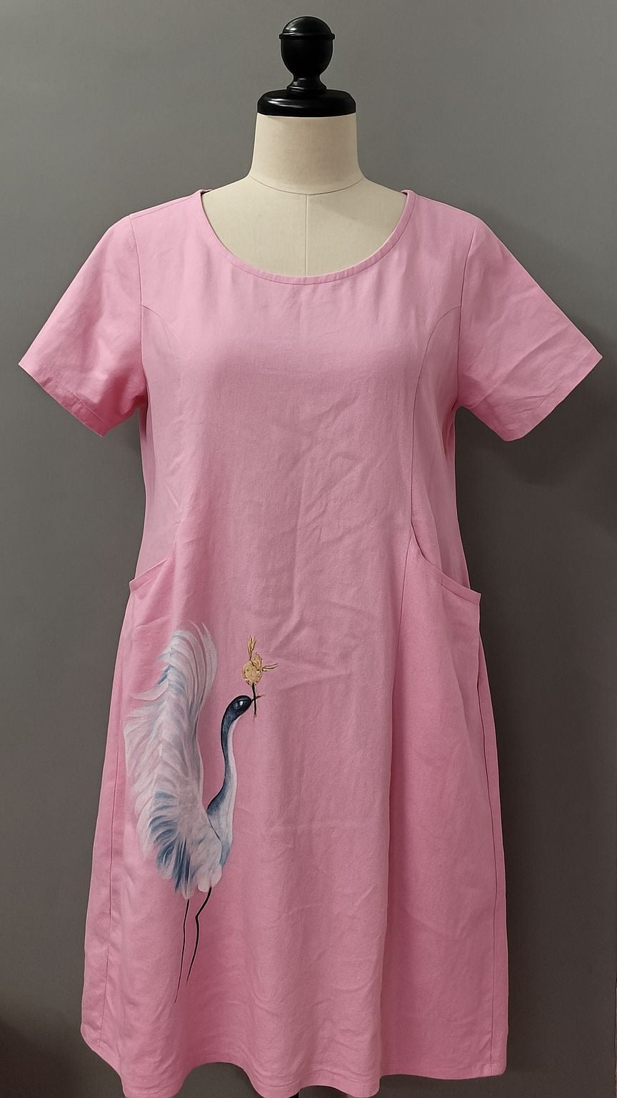 Pink dress with a bird design on a mannequin against a gray background